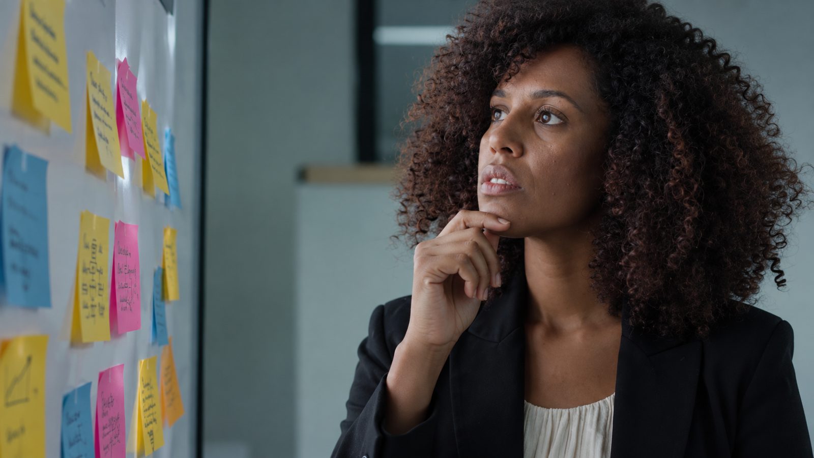 Woman looking thoughtfully at a wall of sticky notes